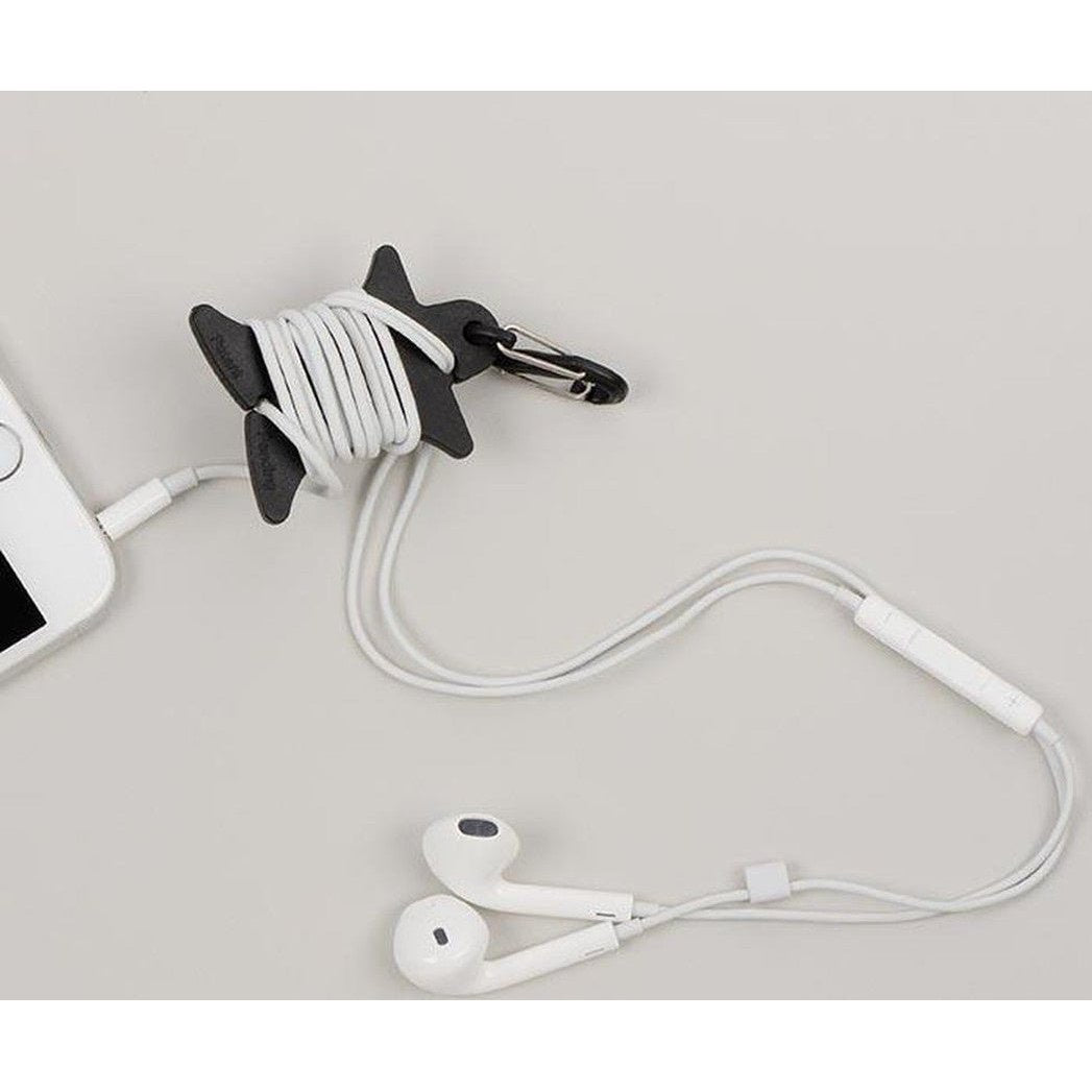 A black Nite Ize Curvyman Cord Supervisor holds a white cord, with white earbuds and a phone visible on a light background.