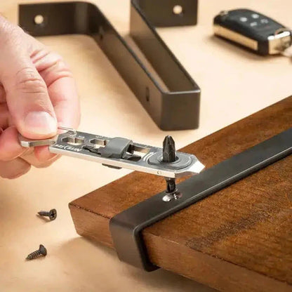 A hand uses the Nite Ize DoohicKey Ratch Key Tool to tighten a screw on a wooden board, with screws and metal brackets visible in the background.