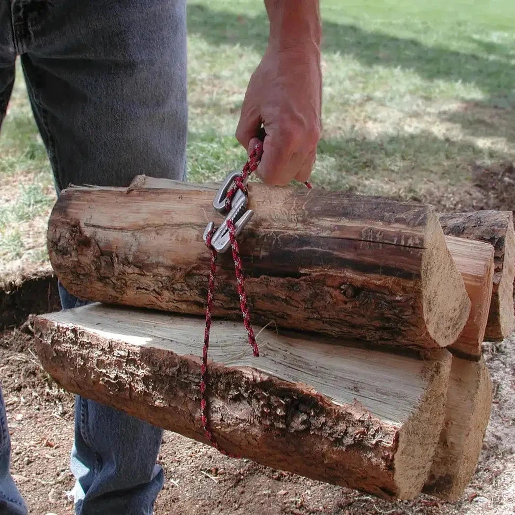 A person holds a stack of logs with a silver Nite Ize Figure 9 Rope Tightener - Small and red rope, outdoors on grass.