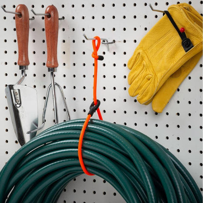 A bright orange Nite Ize Gear Tie Loopable Twist Tie 24 inch - 2 Pack hangs on a pegboard with gardening tools and yellow gloves nearby.