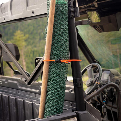 A roll of green netting and a wooden stick are secured with a bright orange Nite Ize Gear Tie Loopable Twist Tie on the side of an off-road vehicle.