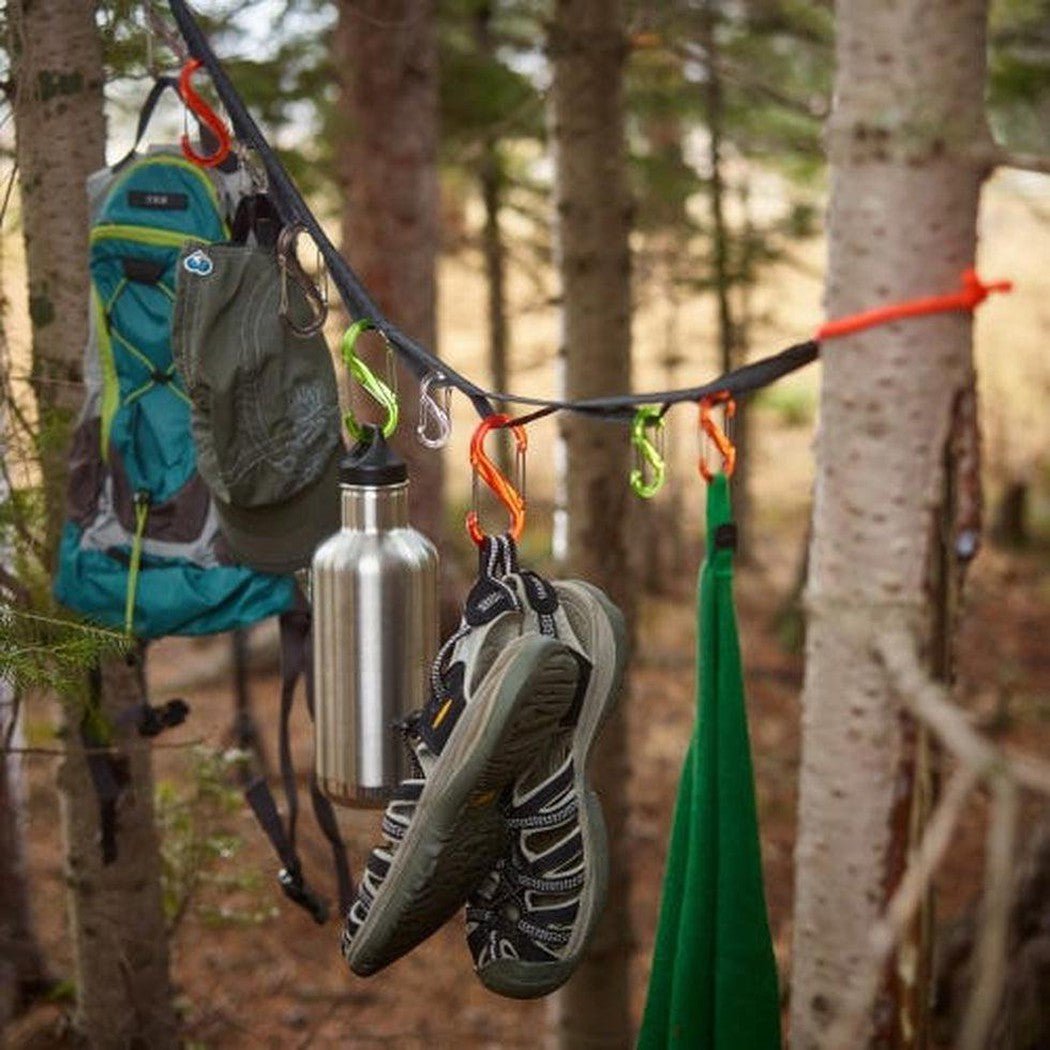 A Nite Ize GearLine Organization System hangs between trees with a backpack, water bottle, and shoes visible.