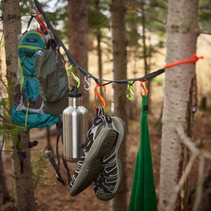 A Nite Ize GearLine Organization System hangs between trees with a backpack, water bottle, and shoes visible.