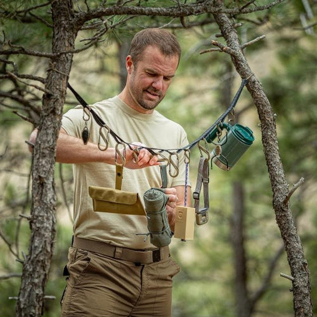 A man in a forest uses the Nite Ize GearLine Organization System hanging from trees.