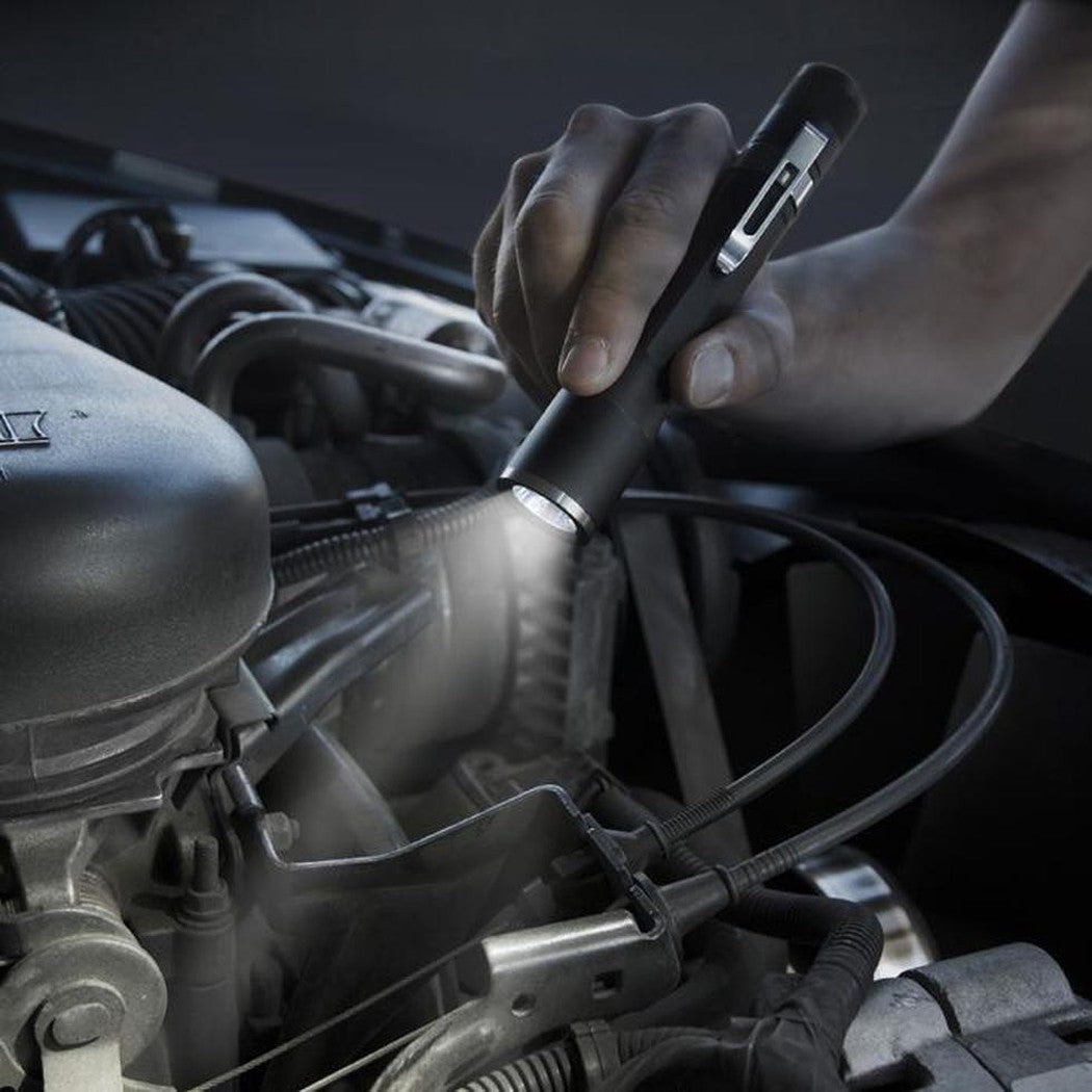 A hand holds the Nite Ize Inova X2 LED Flashlight over a car engine, illuminating the mechanical parts.
