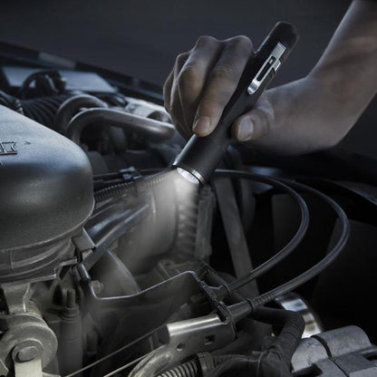 A hand holds the Nite Ize Inova X2 LED Flashlight over a car engine, illuminating the mechanical parts.