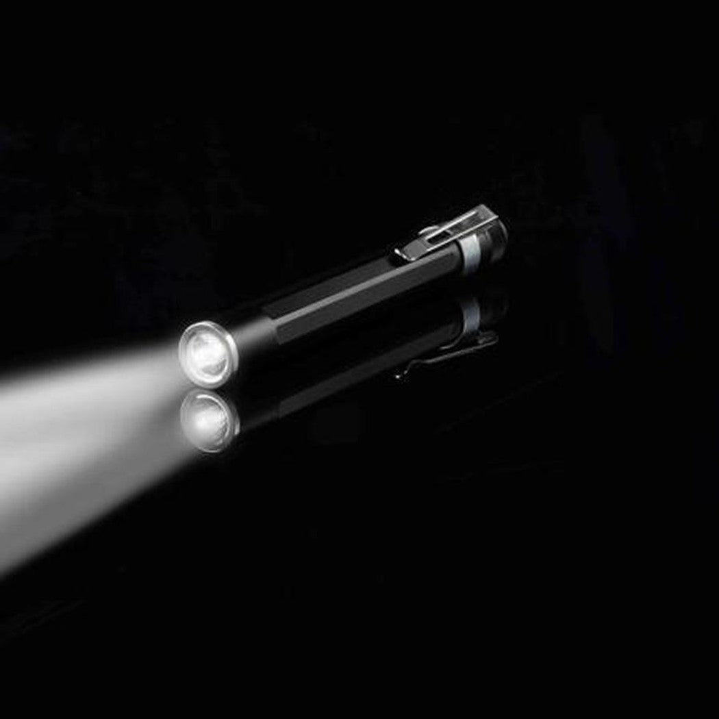 A side view of the Nite Ize Inova XP LED Pen Light with its clip visible, shining a beam of light against a black background.