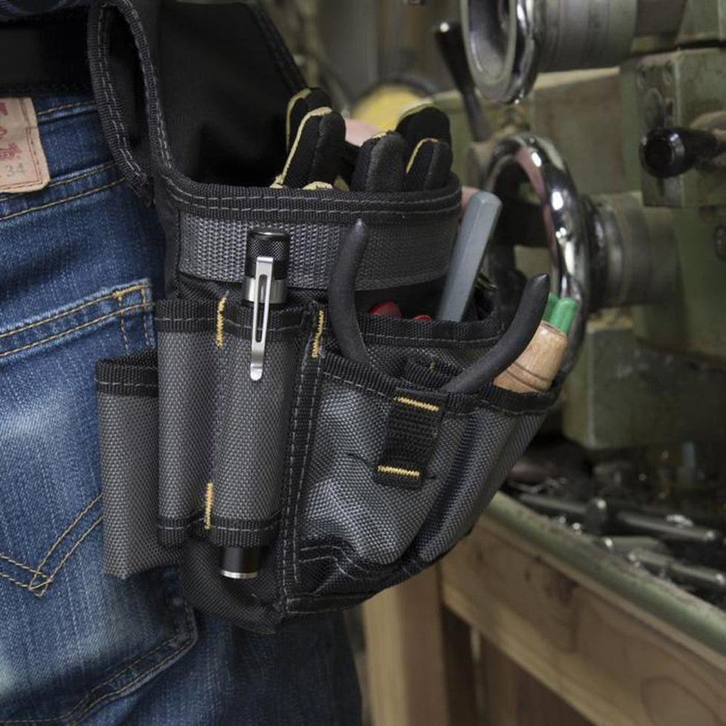 A close-up of the Nite Ize Inova XP LED Pen Light in a black tool pouch attached to blue jeans, with a workshop background.