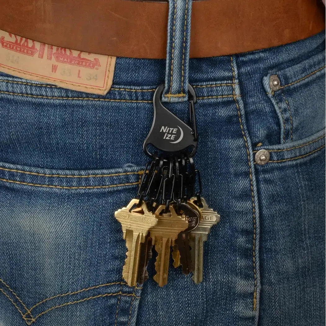 A close-up of a person wearing blue jeans with a black Nite Ize KeyRack Steel S-Binder holding a set of keys attached to their belt loop.