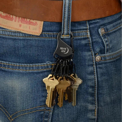 A close-up of a person wearing blue jeans with a black Nite Ize KeyRack Steel S-Binder holding a set of keys attached to their belt loop.
