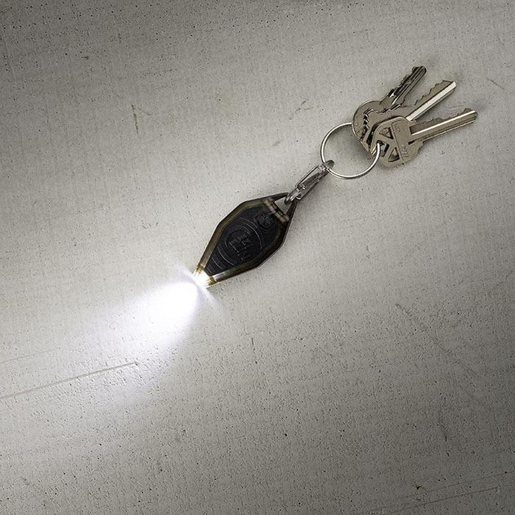 A close-up of the Nite Ize Radiant Rechargeable Microlight in Coyote/WhiteLED on a light gray surface with keys attached.
