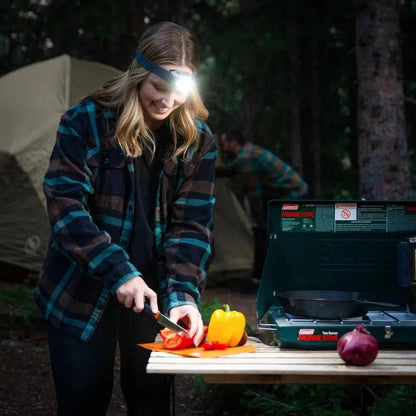 A woman in a plaid shirt uses the Nite Ize Radiant RH1 PowerSwitch Rechargeable Headlamp while camping at night.