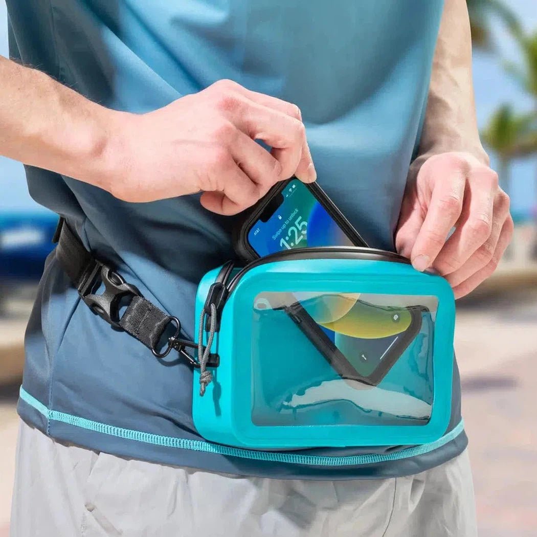 A person puts a phone into the turquoise Nite Ize RunOff Waterproof Hip Pack with a clear window, against a blurred outdoor background.