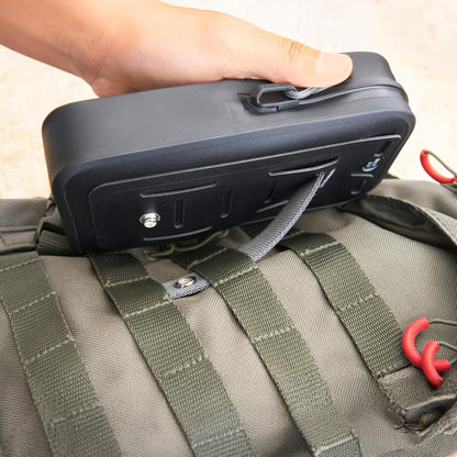 A hand holds the black Nite Ize RunOff Waterproof Phone Case Plus on top of a green backpack with red hooks.