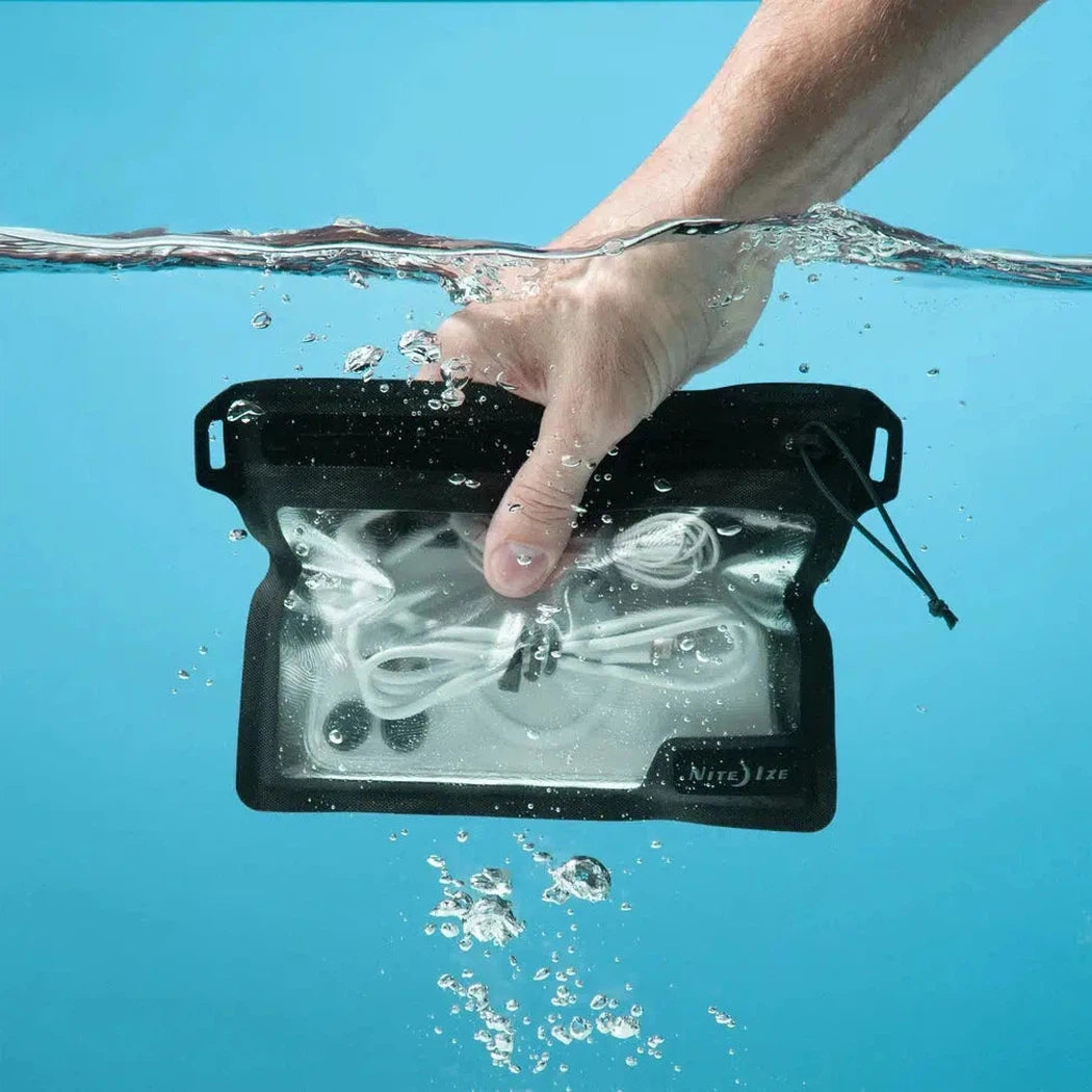 A hand holds the black Nite Ize RunOff Waterproof Pocket underwater with white cords visible inside against a blue background.