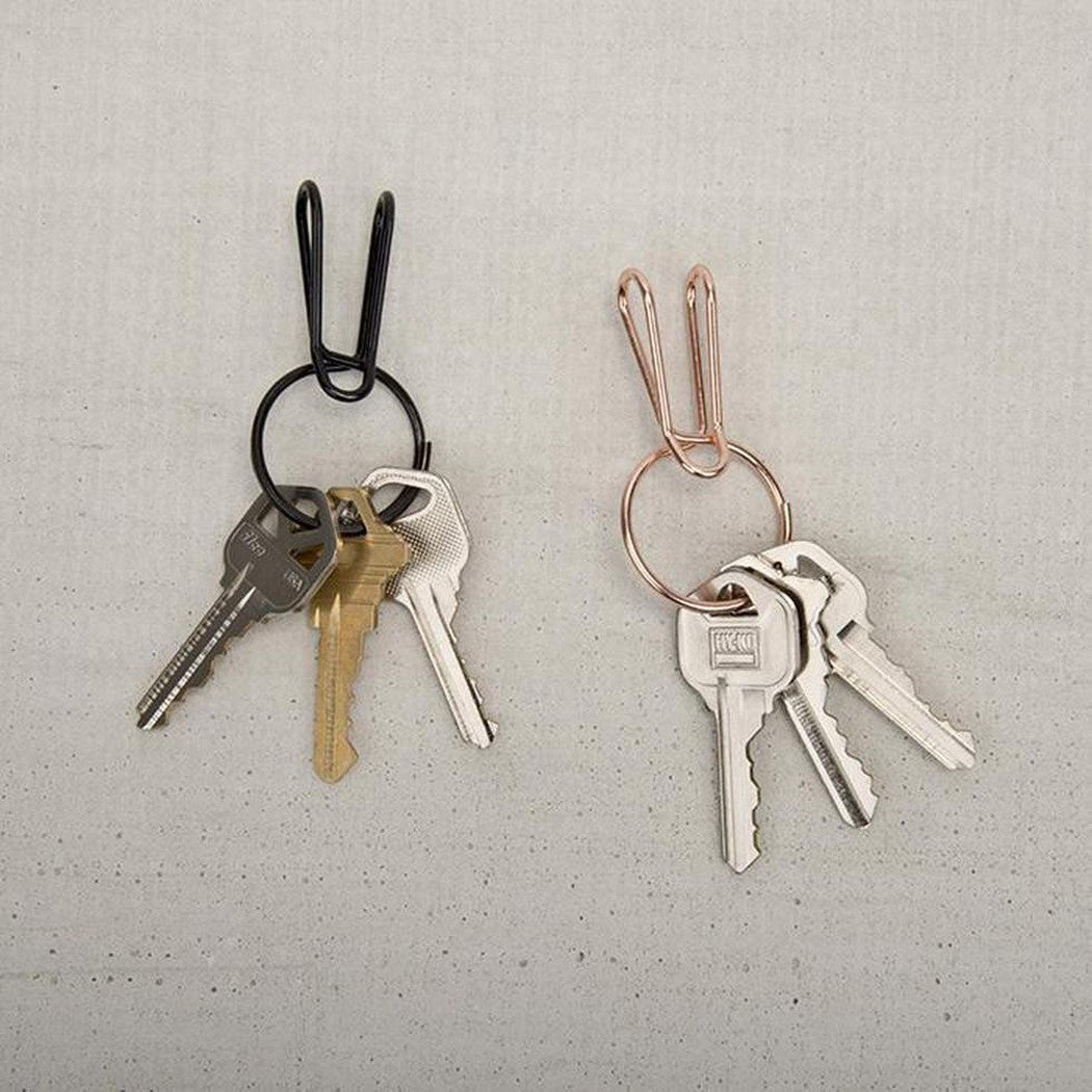 Two Nite Ize SqueezeRing Easy Load Key Clips, one black and one copper, hang on a light gray background with keys attached.