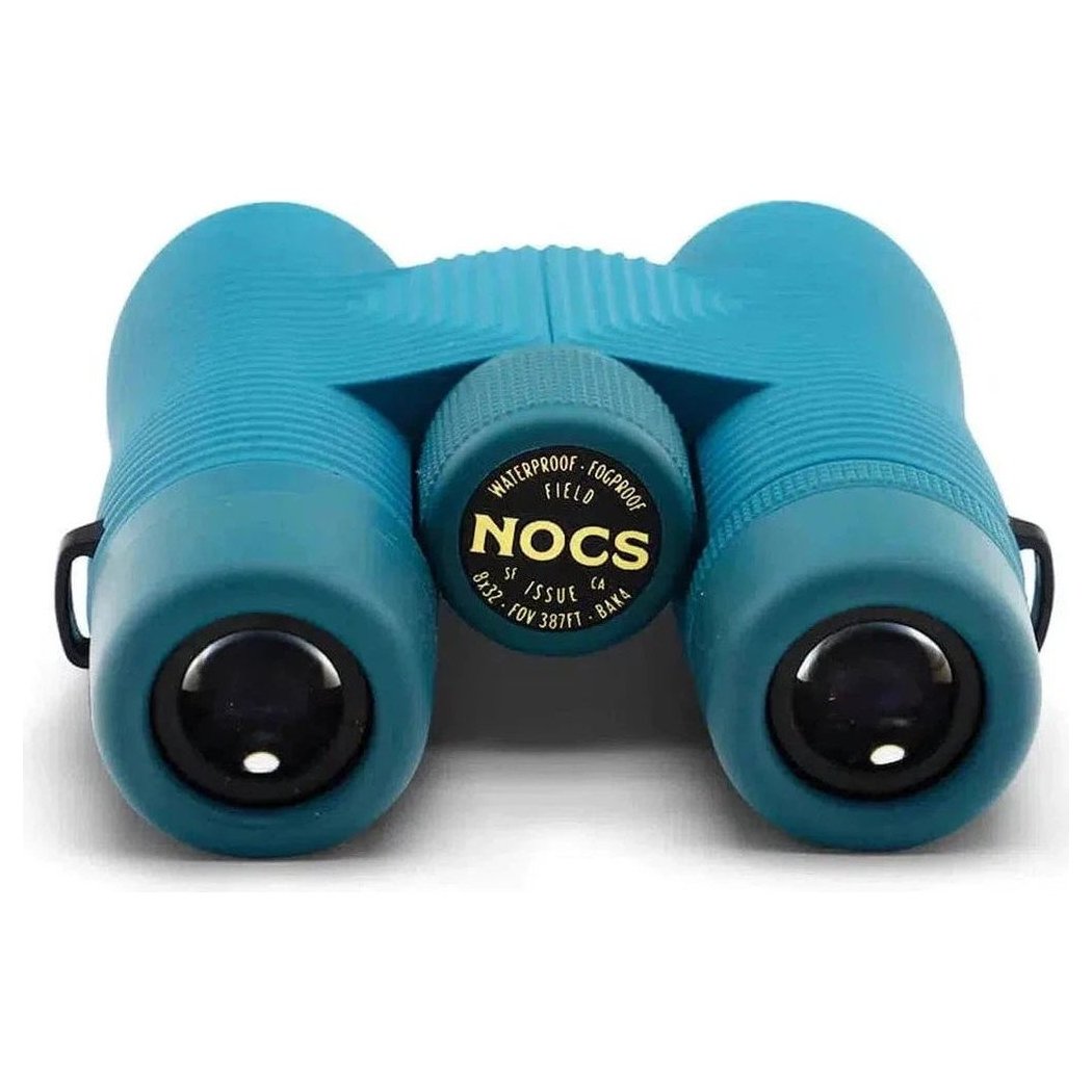Front view of the Nocs Provisions Field Issue Waterproof Binoculars in Corsican Blue showing the central focus wheel and black eyepieces against a white background.