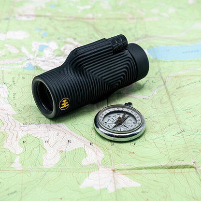 A Tar Pit Black Nocs Provisions Zoom Tube Monocular rests on a topographic map next to a compass.