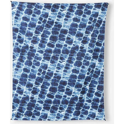 A Nomadix Festival Blanket in Baja Aqua with a blue and white pattern hangs against a white background.