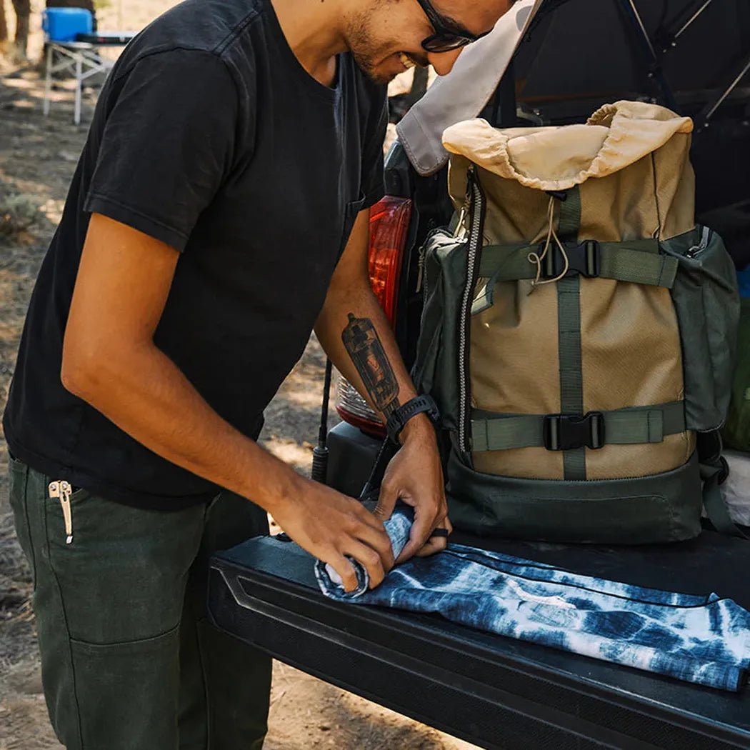 A man folds the Nomadix Ultralight Towel in Agua Blue on a truck bed next to a backpack.