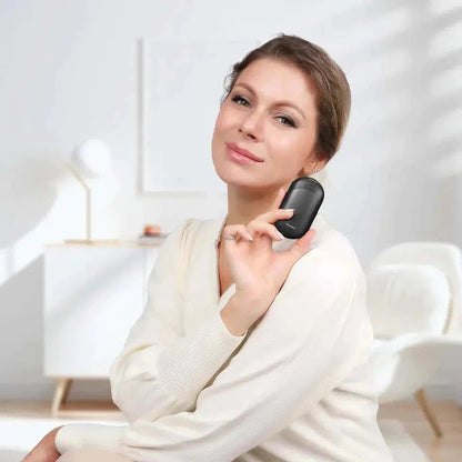 A woman in a white sweater holds the black Ocoopa UT3 Lite Hand Warmer near her neck, with a white chair and cabinet in the background.