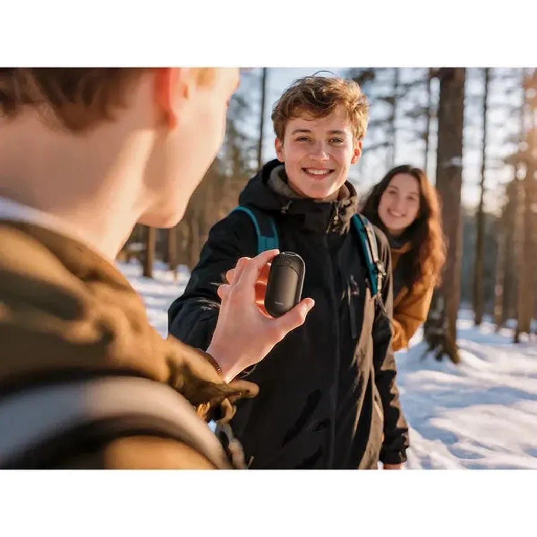 A person shows the Ocoopa UT3 Lite Magnetic Rechargeable Hand Warmers in black to a smiling friend in a snowy forest.