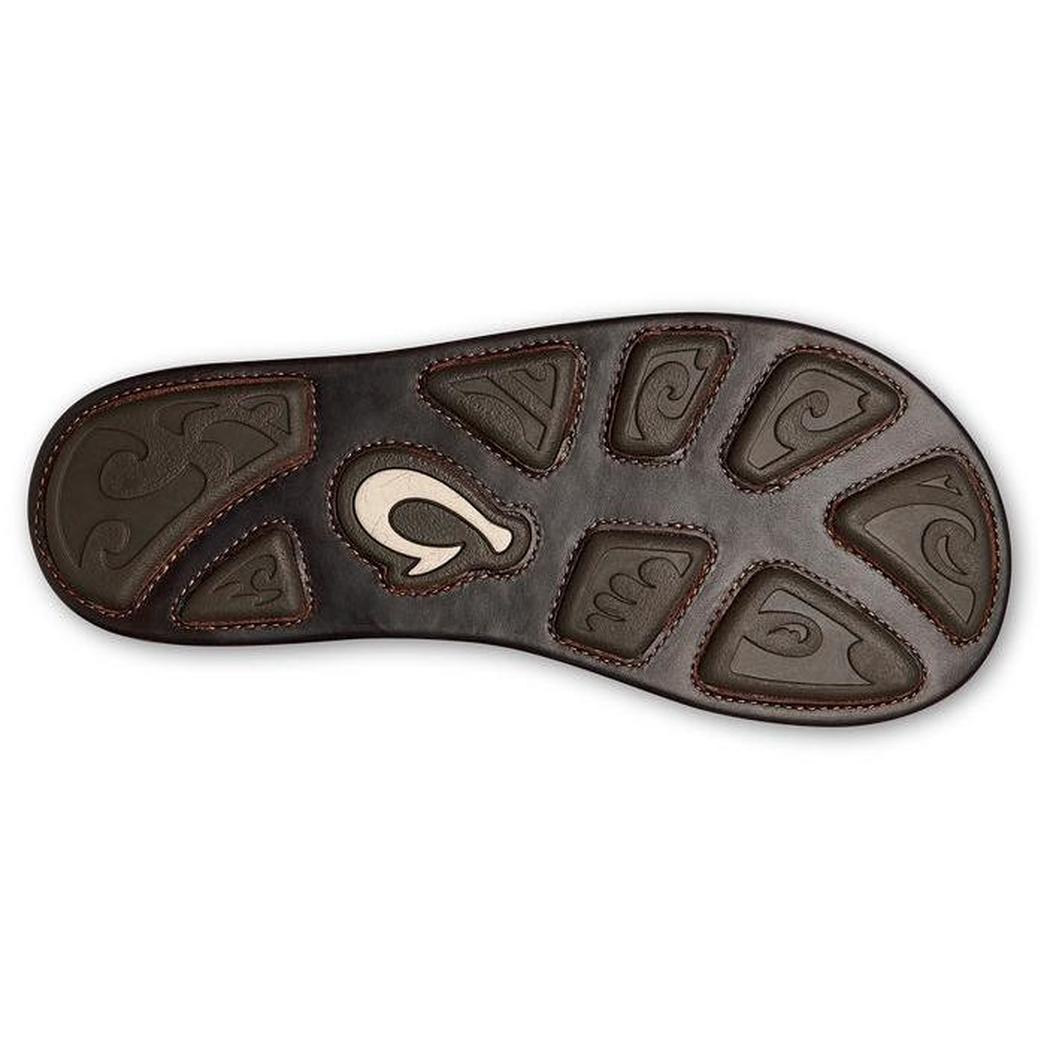 The sole of the Olukai Men's Hikianalia in Tan Dark Java is shown from above, displaying the brand logo and textured tread pattern against a white background.