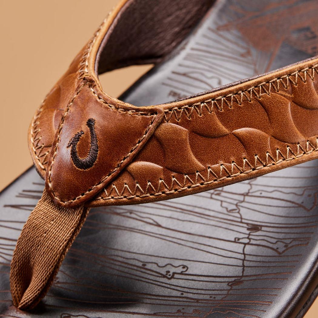 Close-up of the Olukai Men's Hikianalia in Tan Dark Java showing the stitched leather straps and textured footbed against a neutral background.