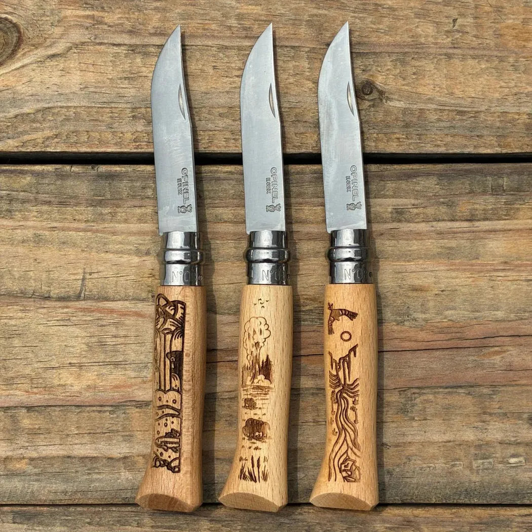 Three Opinel National Parks Collection Grand Canyon knives with engraved handles sit on a wooden surface.