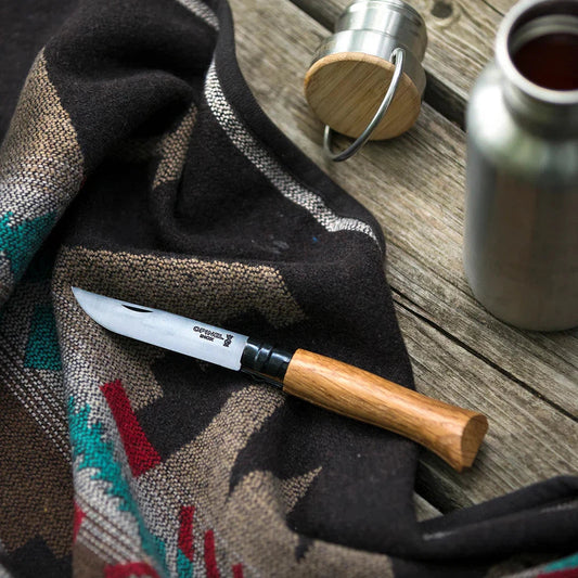 A close-up of the Opinel No.08 Black Oak Folding Knife on a charcoal/ graphite patterned cloth with a wooden table background.