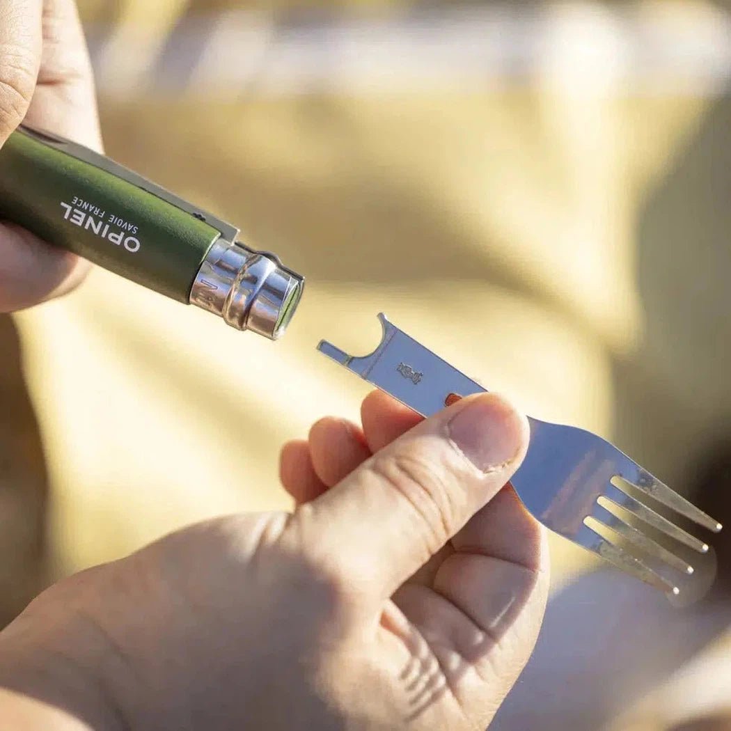 A hand holds the green Opinel Picnic Plus Cutlery Insert near a fork, showing the detachable design against a light background.