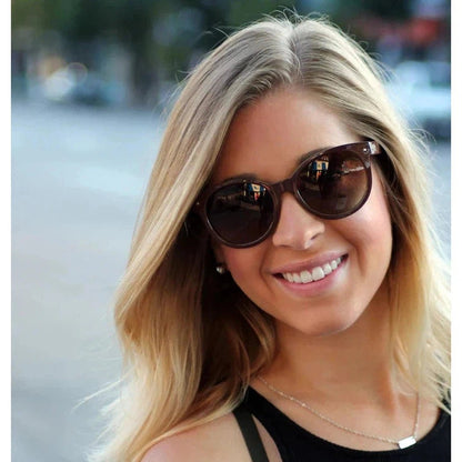 A woman smiles wearing the Optic Nerve Hotplate sunglasses with a street background.