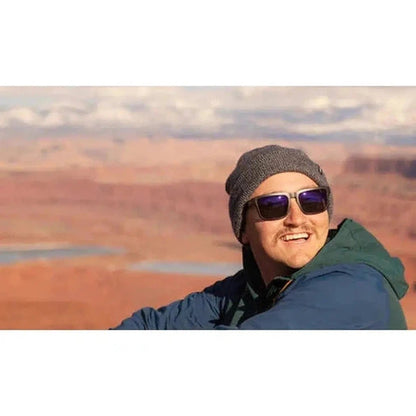 A smiling model wears the Optic Nerve Mashup sunglasses in Matte Black + Wood against a desert landscape.
