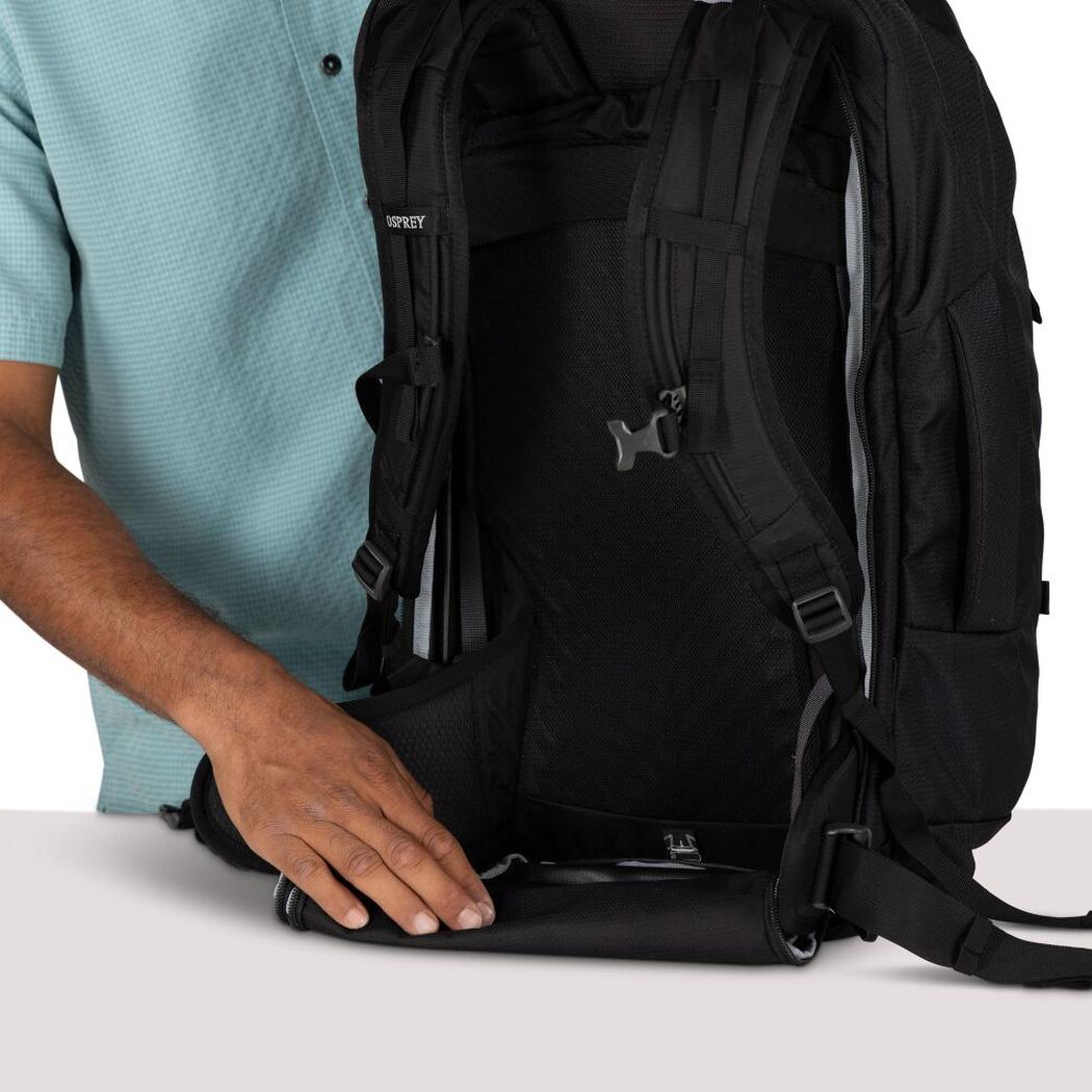 A person in a light blue shirt holds the bottom of a black Osprey Farpoint 55 backpack against a white background.