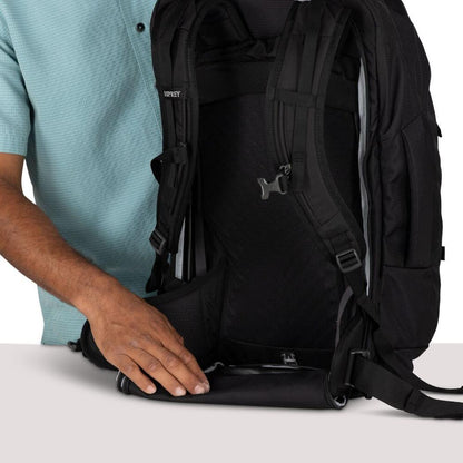 A person in a light blue shirt holds the bottom of a black Osprey Farpoint 55 backpack against a white background.