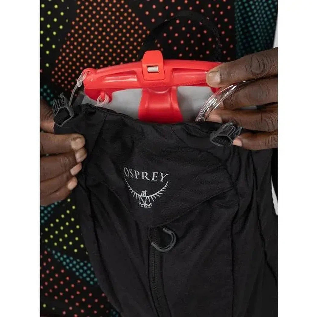 A close-up of the Osprey Katari 7 hydration pack in black, showing the red reservoir and the Osprey logo on the front pocket, with a colorful dotted background.