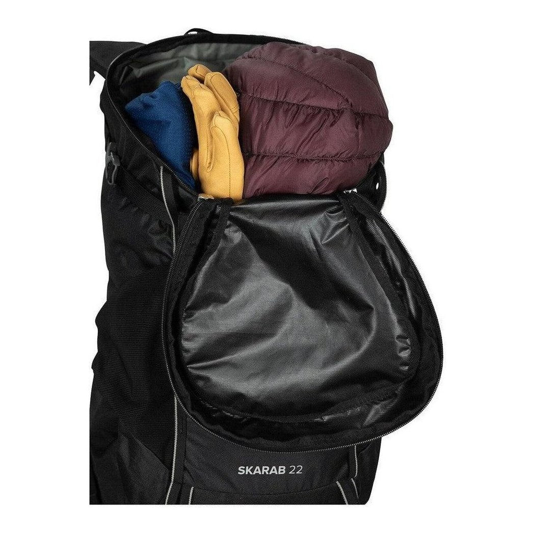 Side view of the Osprey Skarab 22 in Tundra Green showing the front pocket and gear inside against a white background.