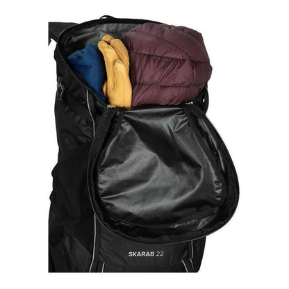 Side view of the Osprey Skarab 22 in Tundra Green showing the front pocket and gear inside against a white background.