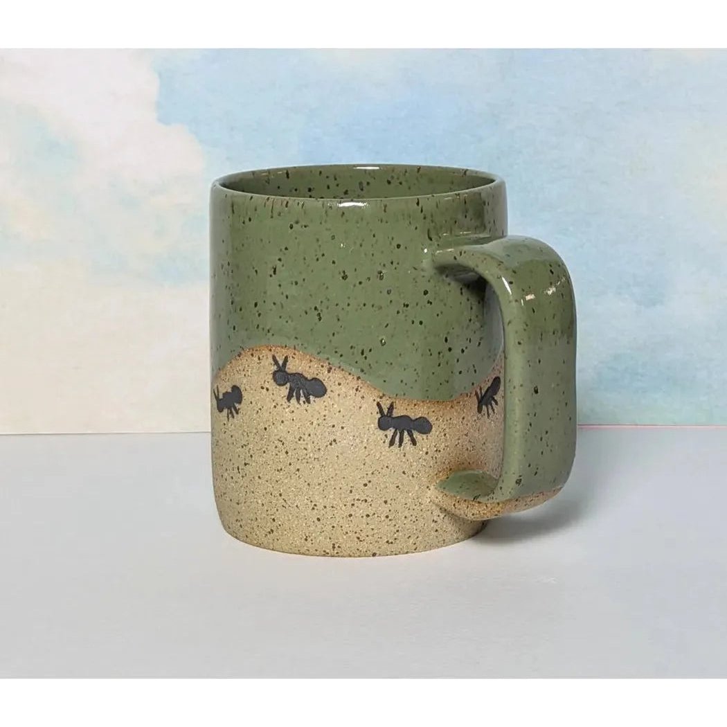 A side view of the Osso Ceramics Ants On A Hill Mug showing the ant design against a light blue background.