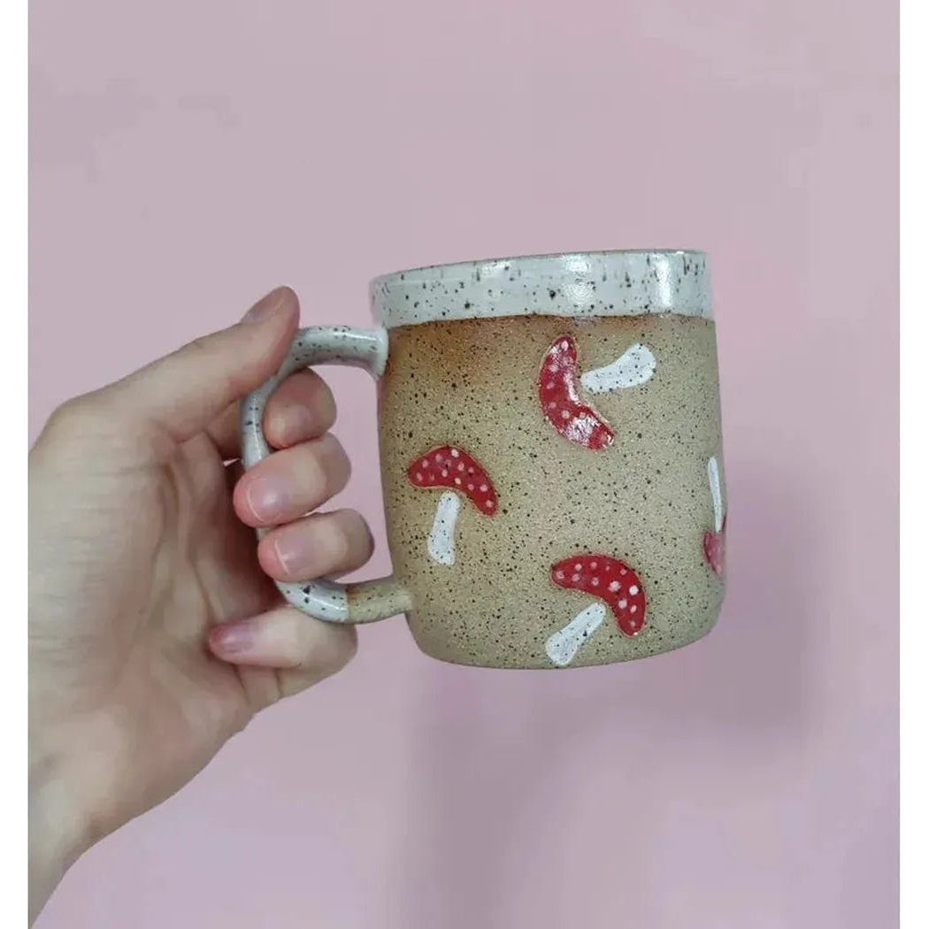 A hand holds the Osso Ceramics Mushroom Stamp Mug against a pink background.