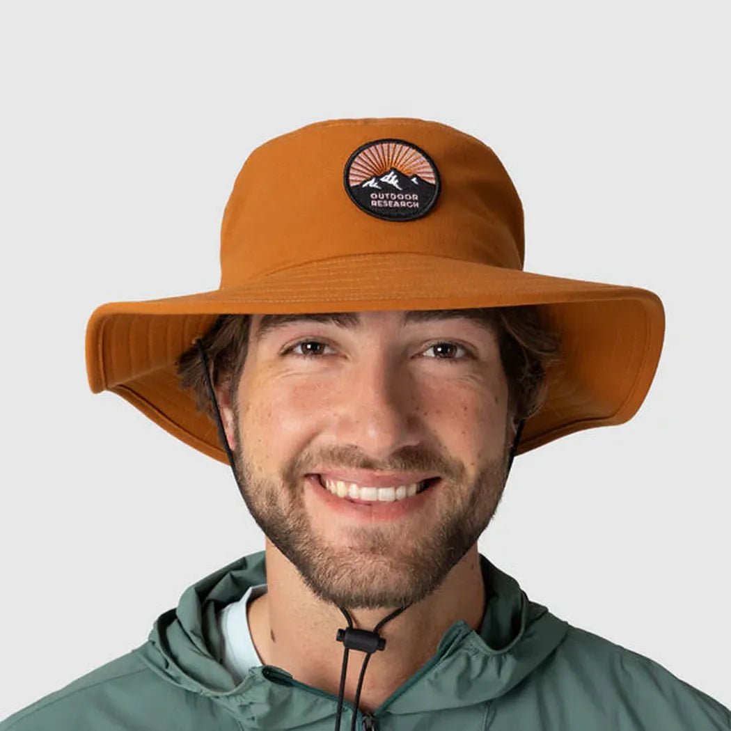 A front view of the Outdoor Research Heyday Boonie Hat in Dark Sedona on a model wearing a green jacket against a plain background.