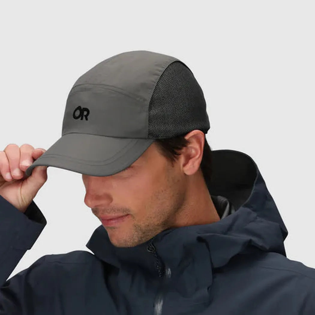 A man wearing the Outdoor Research Swift Cap in Black/Dark Grey adjusts it while wearing a dark jacket against a plain background.