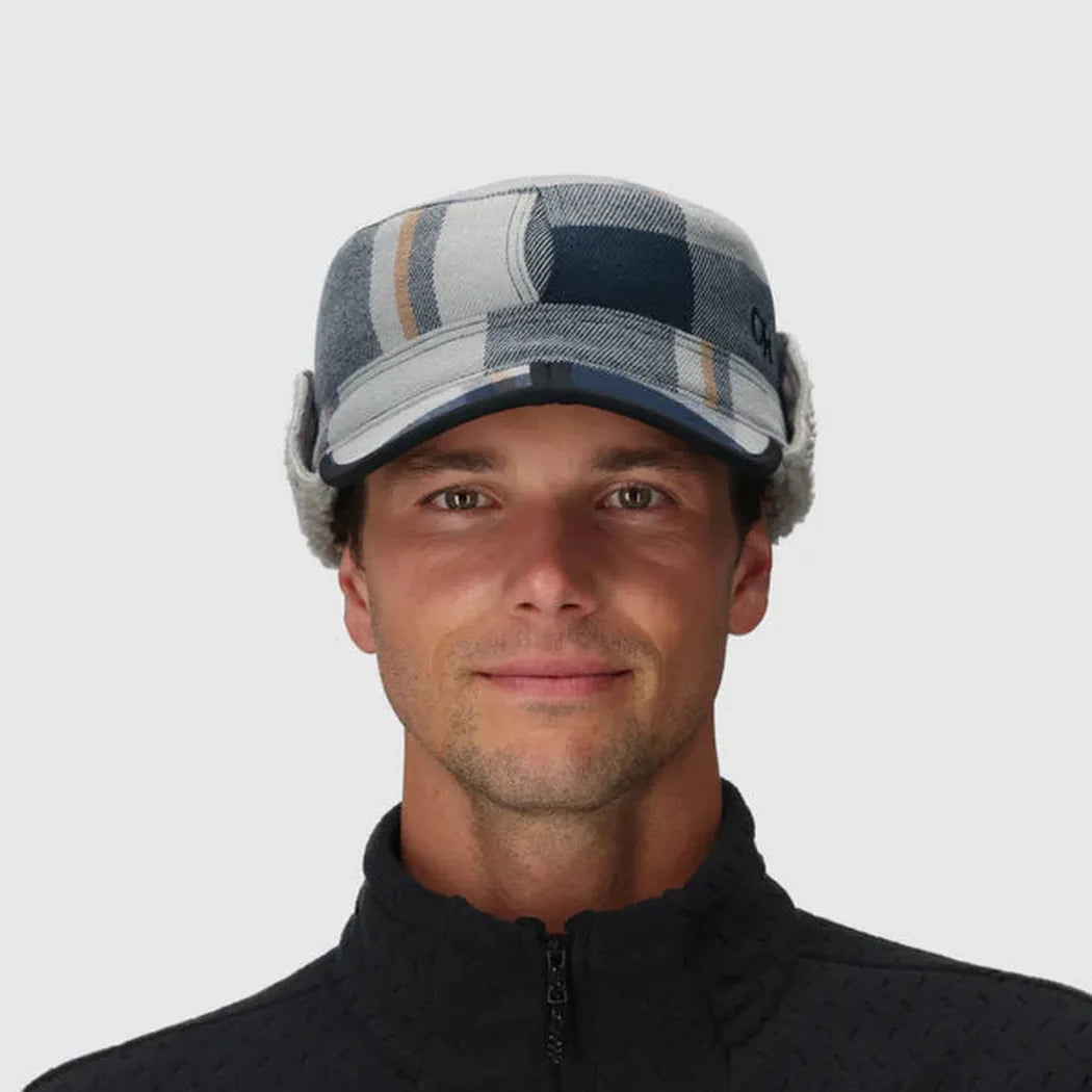 A front view of the Outdoor Research Yukon Cap in Black/Pewter Plaid on a model wearing a black zip-up jacket against a plain white background.