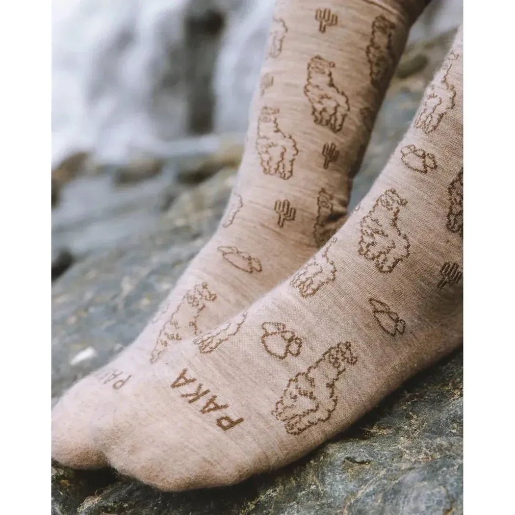 Light grey Paka Apparel Essential Sebastian Crew Socks with alpaca and cactus prints on feet resting on a rock.