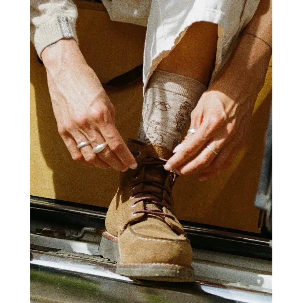 A person tying a brown hiking boot while wearing Paka Apparel Essential Sebastian Crew Socks in Light Grey.