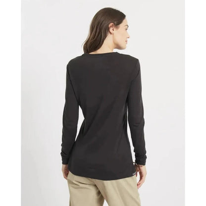 Back view of the Paka Apparel Women's Aire Long Sleeve in Black on a model wearing khaki pants against a plain white background.