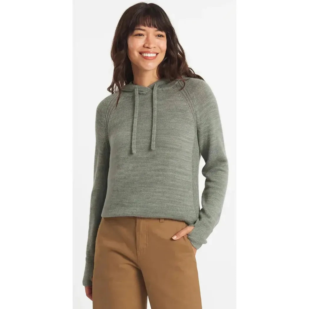 A woman wearing the Paka Apparel Women's Hoodie in Willow stands against a plain white background with one hand in her pocket.