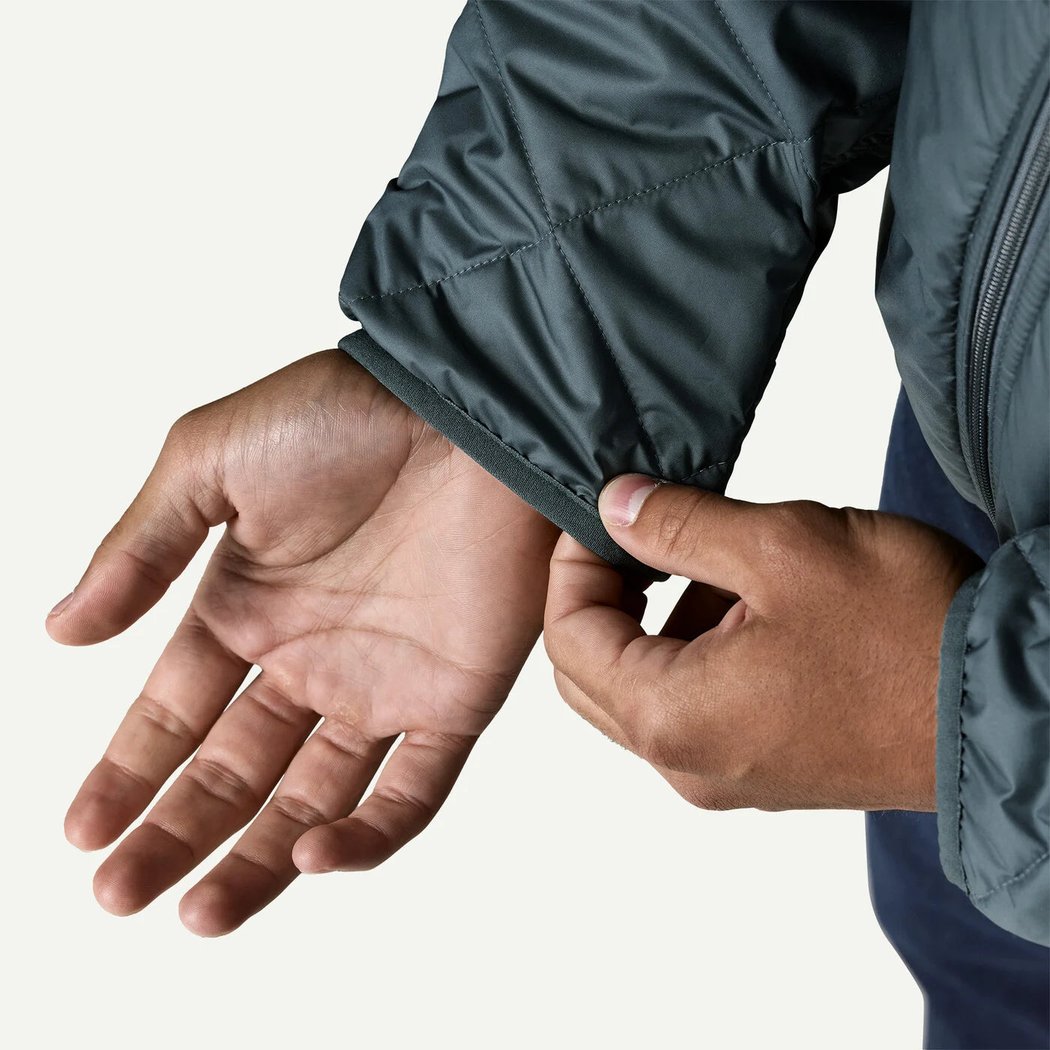 A person adjusts the cuff of the Patagonia Men's Diamond Quilted Bomber Hoody in Summit Blue against a plain white background.