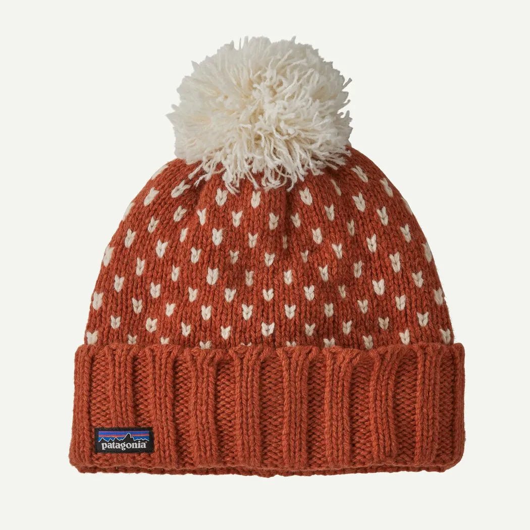 A front view of the Patagonia Snowbelle Beanie in Burnished Red with a white pom pom and ribbed cuff, displayed against a plain white background.