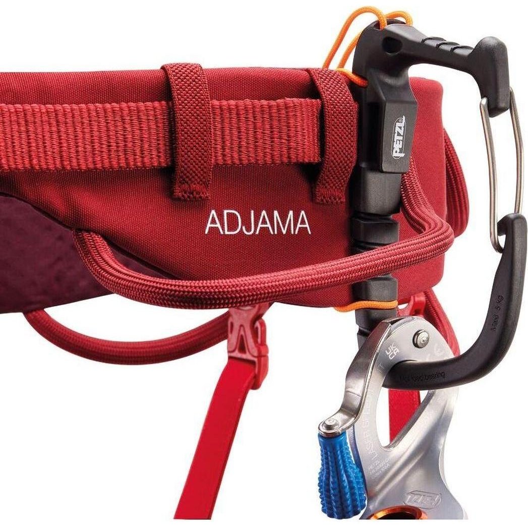 A close-up of the Petzl Adjama dark red climbing harness showing the buckle and carabiner attachment points.